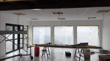 Grande pièce en cours de travaux, baies vitrées, ossature de faux plafond apparente et tréteaux au sol, avant passage des réseaux.