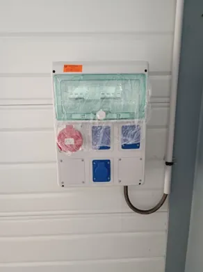 Coffret de chantier posé sur un bardage métallique, capot vert transparent, prises de courant et alimentation souple raccordée en partie basse.
