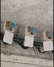 Trois boîtes de dérivation alignées sur un mur en parpaing brut, alimentées par un chemin de câbles multicolore.