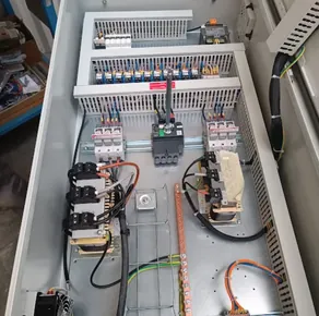 Grande armoire industrielle ouverte sur établi : disjoncteurs de forte intensité, contacteurs et jeux de barres en cuivre.