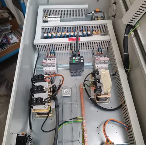 Grande armoire industrielle ouverte sur établi : disjoncteurs de forte intensité, contacteurs et jeux de barres en cuivre.