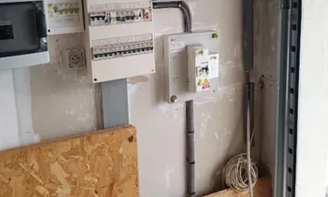Mur de garage : deux tableaux de protections modulaires, coffret de commande, cheminement en apparent et couronne de câble au sol.
